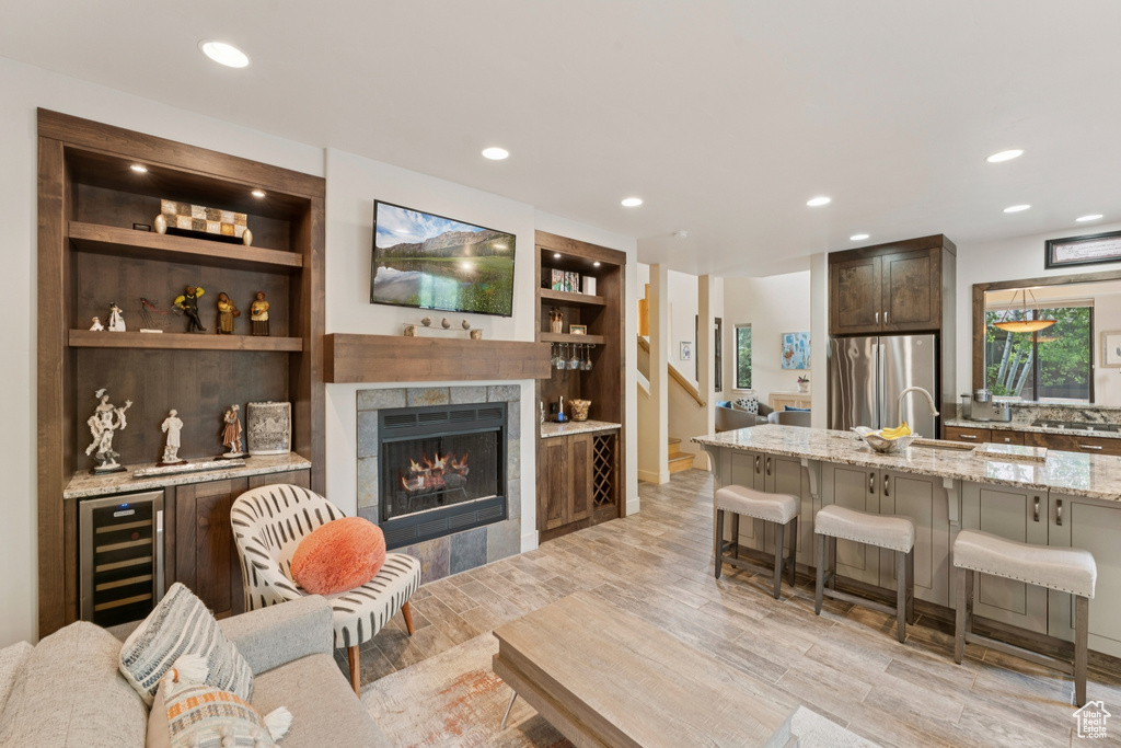 Living area featuring beverage cooler, recessed lighting, light wood-type flooring, a tiled fireplace, and built in features