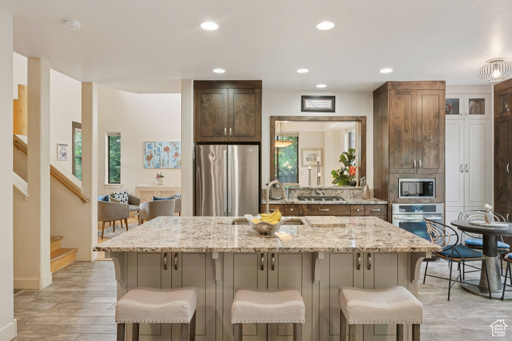 Kitchen featuring appliances with stainless steel finishes, a kitchen bar, recessed lighting, light stone counters, and a center island with sink