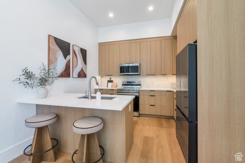 Kitchen with stainless steel appliances, a sink, light brown cabinets, modern cabinets, and a breakfast bar area