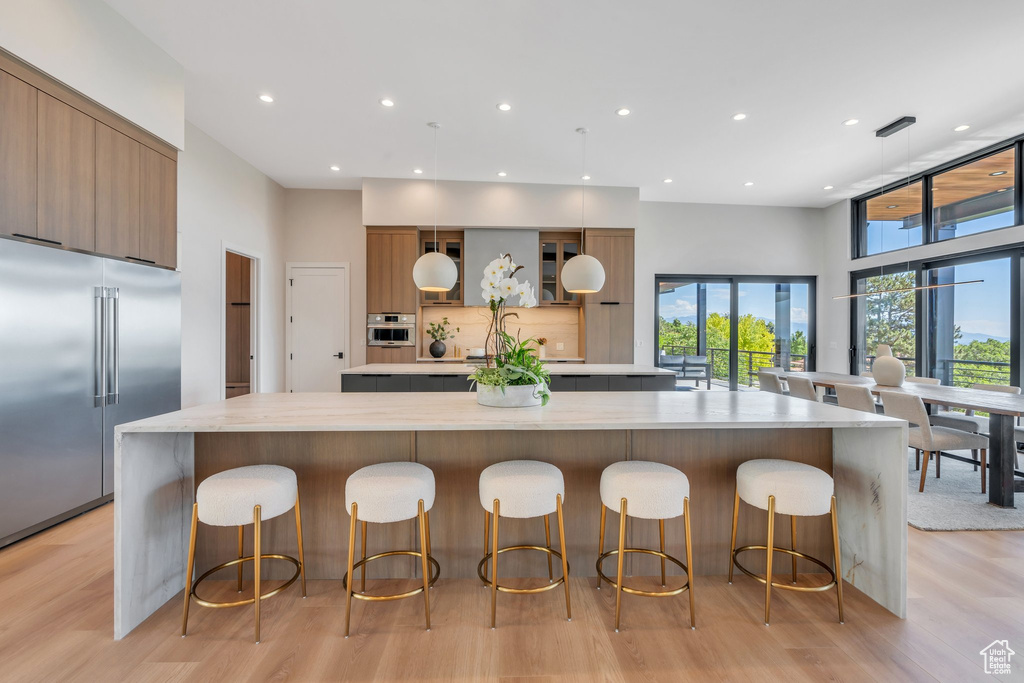 Kitchen with appliances with stainless steel finishes, a large island, modern cabinets, light countertops, and light wood finished floors