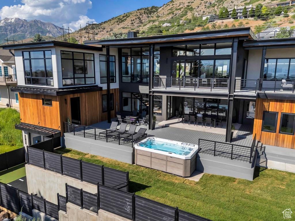 Back of house with a hot tub, a mountain view, a patio, and a balcony