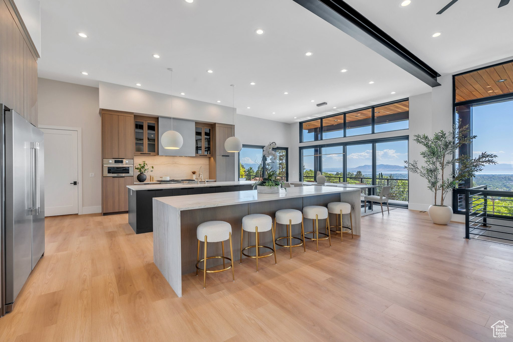 Kitchen with appliances with stainless steel finishes, a large island with sink, modern cabinets, light wood-style flooring, and light countertops