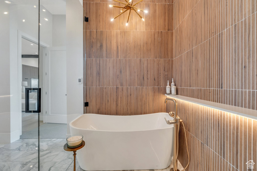 Full bath featuring a soaking tub, a chandelier, marble tiled flooring, and tile walls