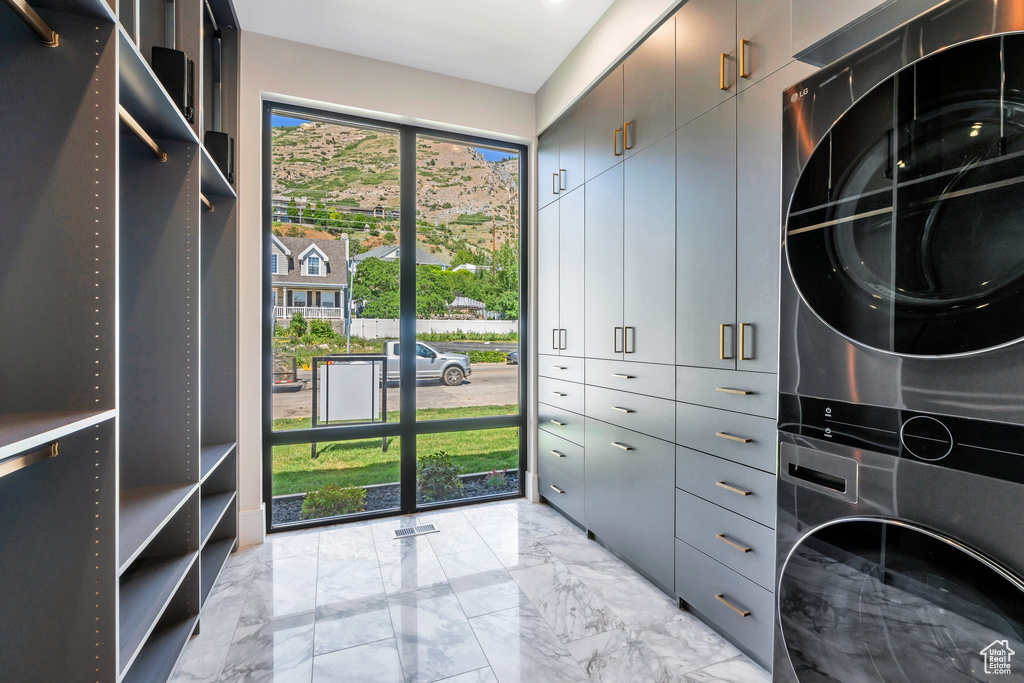 Spacious closet featuring stacked washing machine and dryer and light marble finish floors