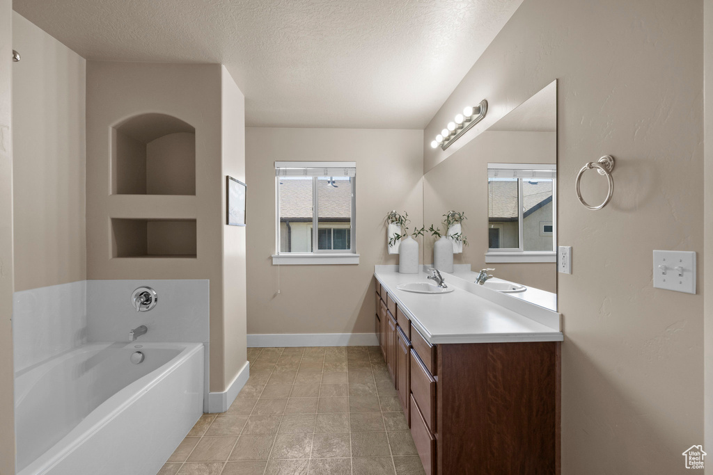 Full bath with double vanity, healthy amount of natural light, a bath, a textured ceiling, and baseboards