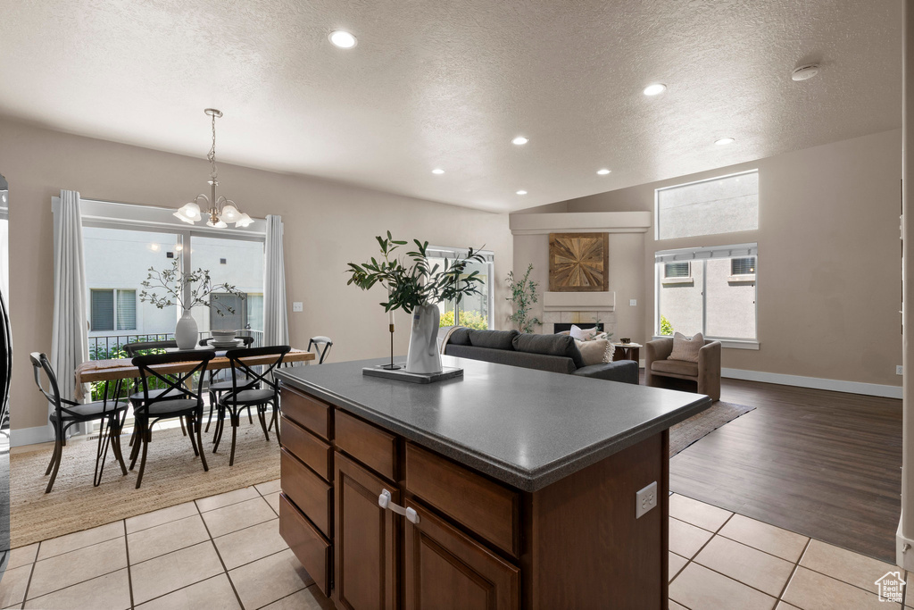 Kitchen with dark countertops, a textured ceiling, a kitchen island, light tile patterned floors, and a chandelier
