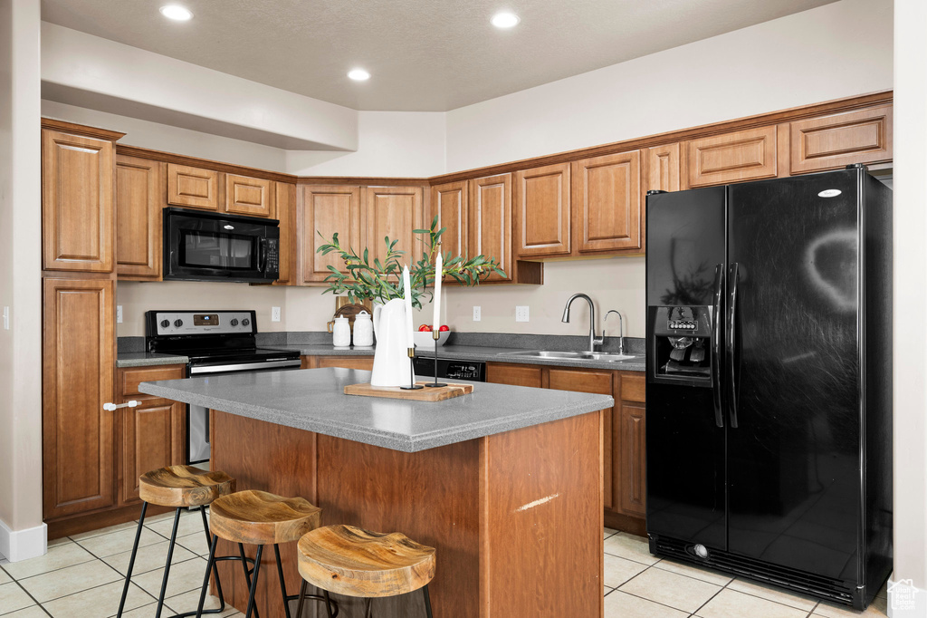 Kitchen featuring black appliances, a sink, light tile patterned floors, a center island, and a breakfast bar