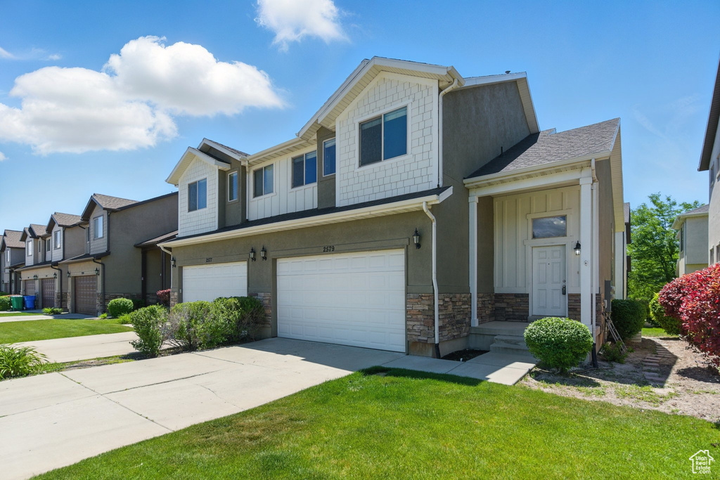 View of property featuring stone siding, an attached garage, board and batten siding, a front lawn, and a residential view