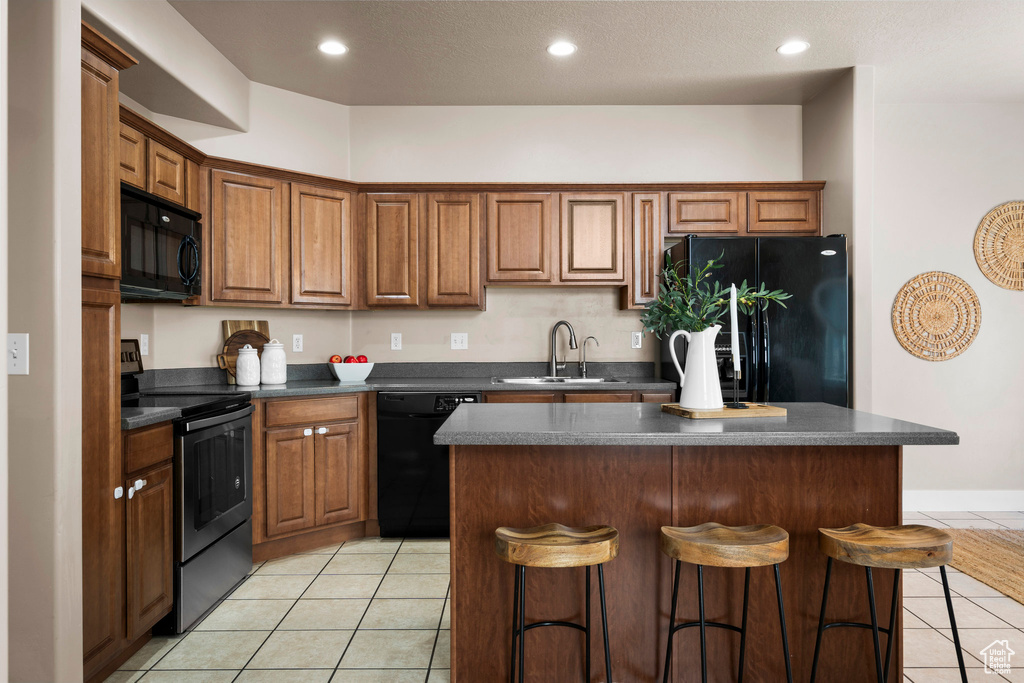 Kitchen featuring black appliances, a sink, light tile patterned flooring, dark countertops, and a breakfast bar
