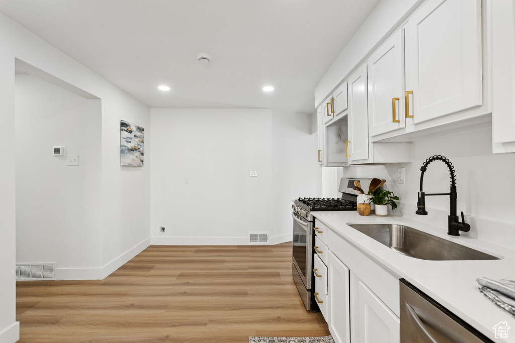 Kitchen featuring appliances with stainless steel finishes, a sink, recessed lighting, white cabinetry, and light countertops