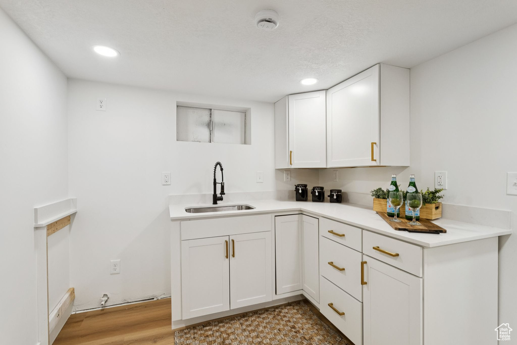 Kitchen featuring a sink, light countertops, white cabinetry, recessed lighting, and light wood-style floors