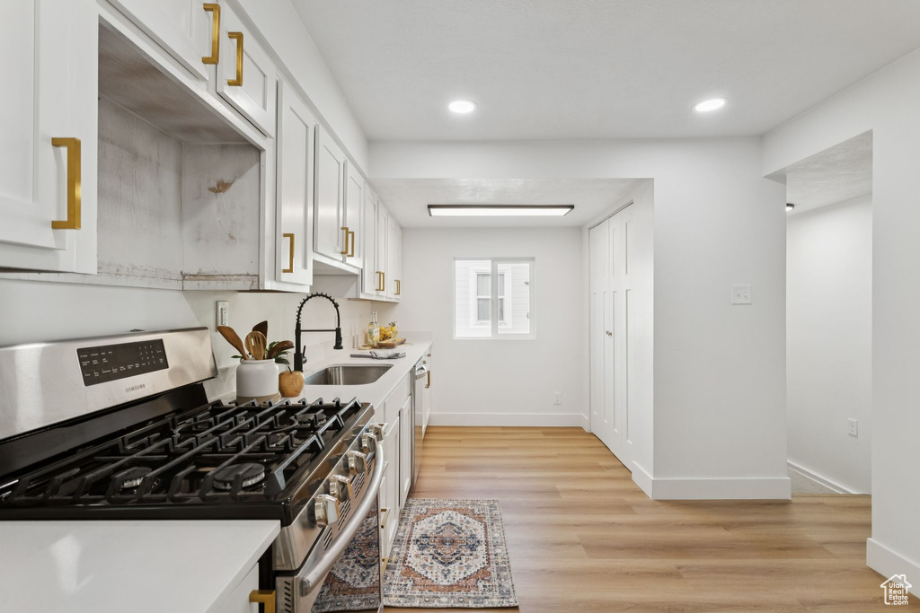 Kitchen with stainless steel appliances, a sink, light wood-type flooring, light countertops, and white cabinetry