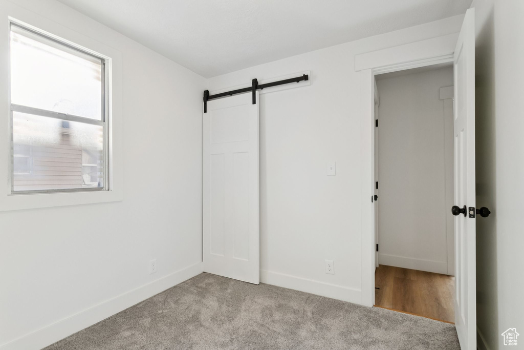 Unfurnished bedroom featuring baseboards, light carpet, and a barn door