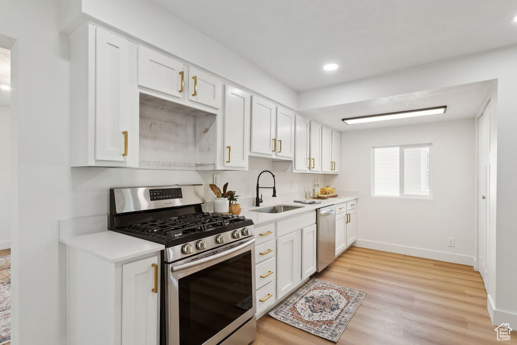 Kitchen with appliances with stainless steel finishes, a sink, light countertops, baseboards, and recessed lighting