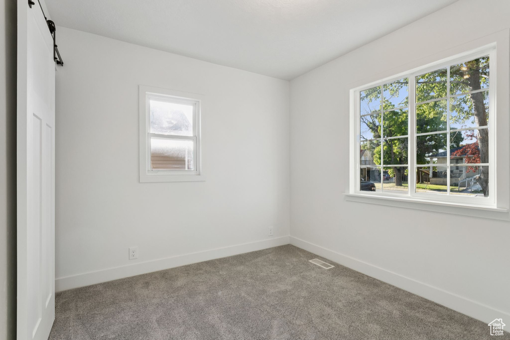 Unfurnished bedroom featuring multiple windows, carpet flooring, baseboards, and a barn door