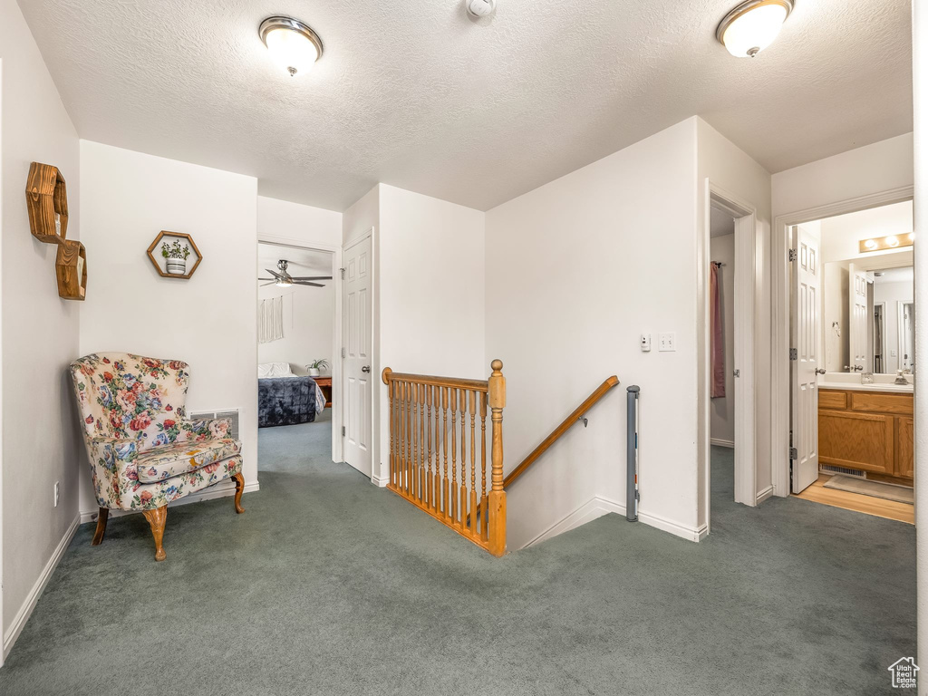 Hallway with an upstairs landing, carpet flooring, baseboards, and a textured ceiling
