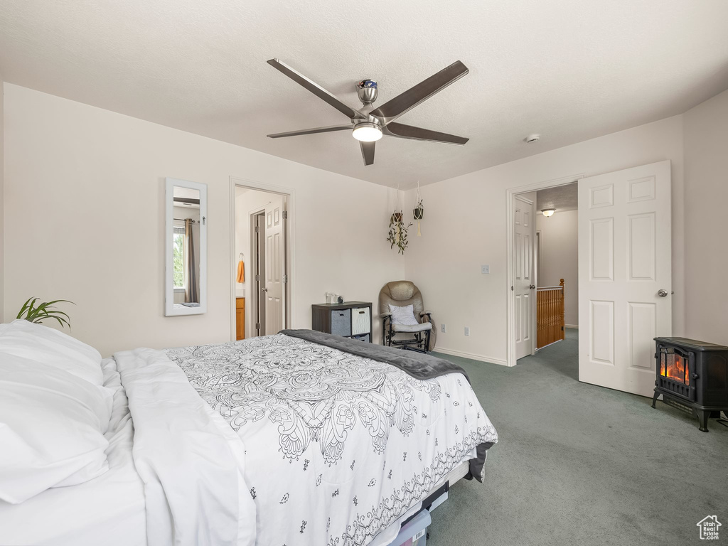 Carpeted bedroom with a wood stove, ceiling fan, and baseboards