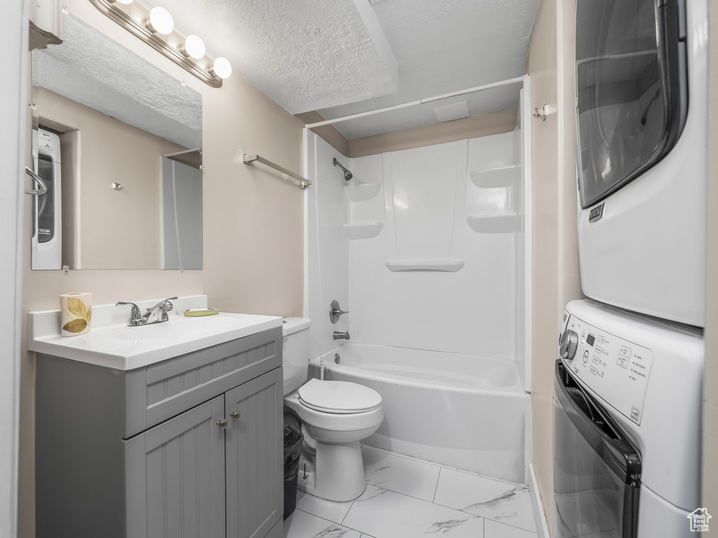 Bathroom with estacked washer and dryer, toilet, vanity, marble finish flooring, and shower / bath combination