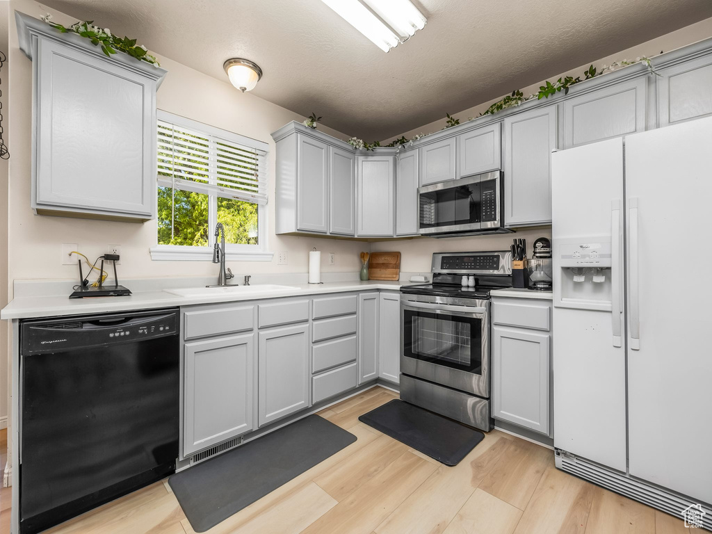 Kitchen with stainless steel appliances, a sink, light wood-style flooring, gray cabinetry, and light countertops