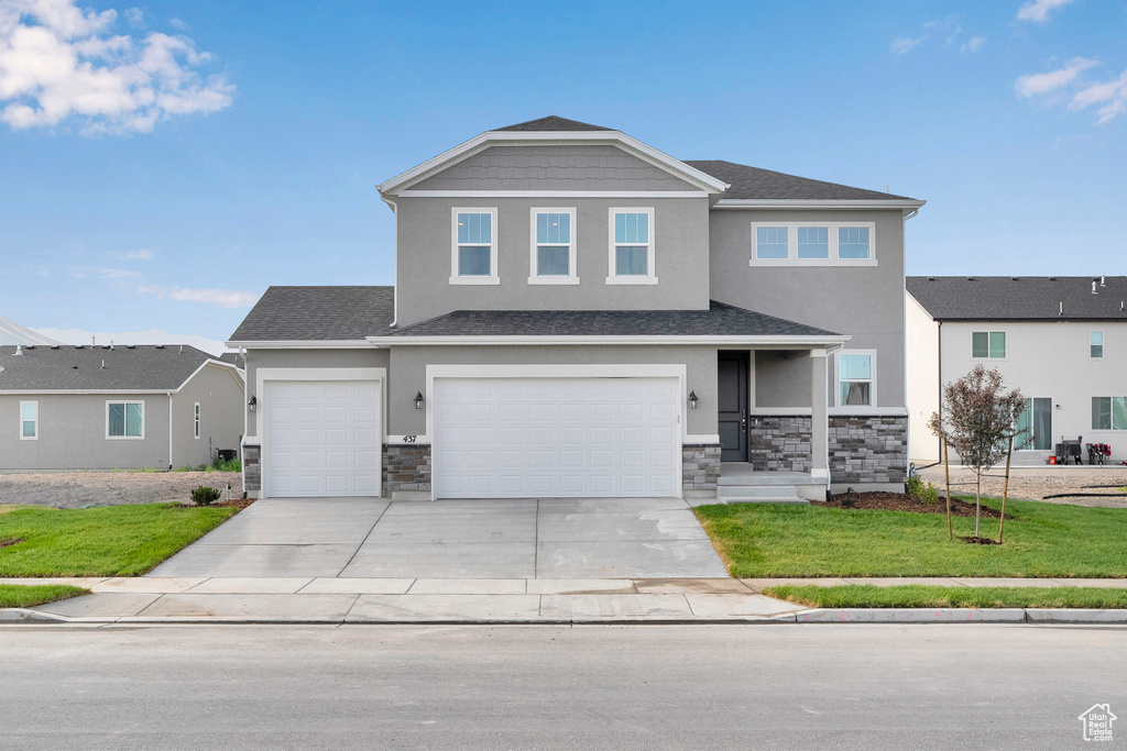 View of front facade featuring stucco siding, stone siding, concrete driveway, a front yard, and an attached garage