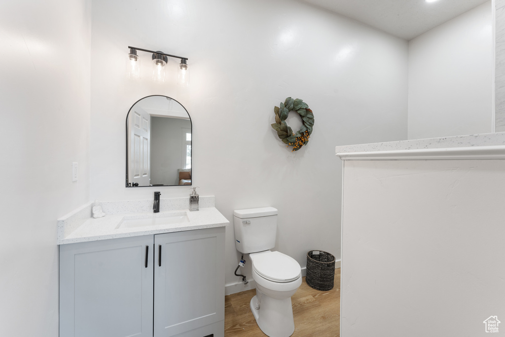 Half bath featuring toilet, wood finished floors, vanity, and baseboards