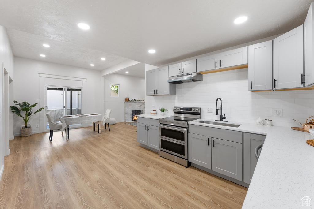 Kitchen featuring range with two ovens, a sink, gray cabinetry, under cabinet range hood, and decorative backsplash