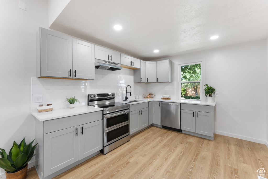 Kitchen featuring appliances with stainless steel finishes, under cabinet range hood, gray cabinets, tasteful backsplash, and a sink