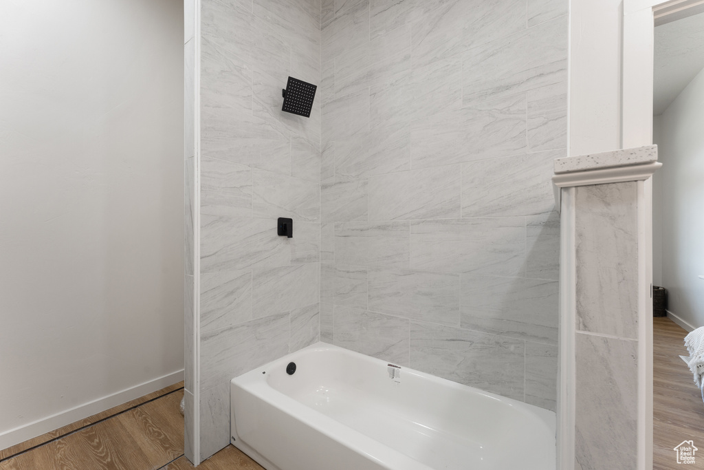 Full bath featuring baseboards, wood finished floors, and washtub / shower combination