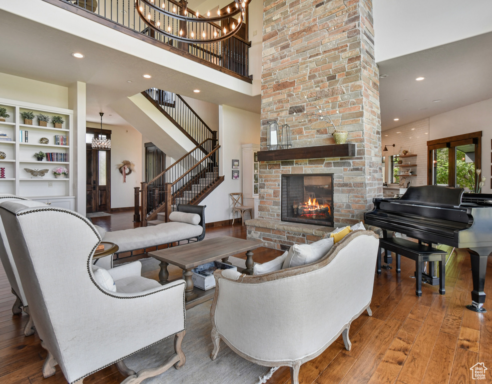 Living area with hardwood / wood-style flooring, a towering ceiling, a chandelier, a large fireplace, and recessed lighting
