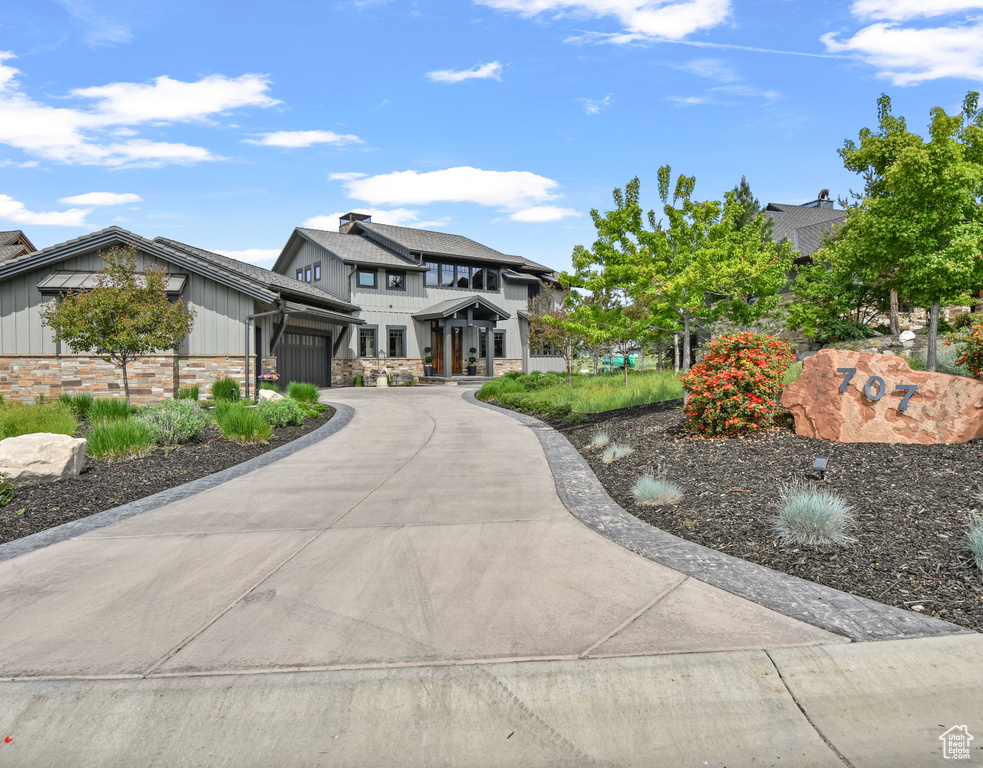 View of front of home with a garage, asphalt driveway, stone siding, and board and batten siding