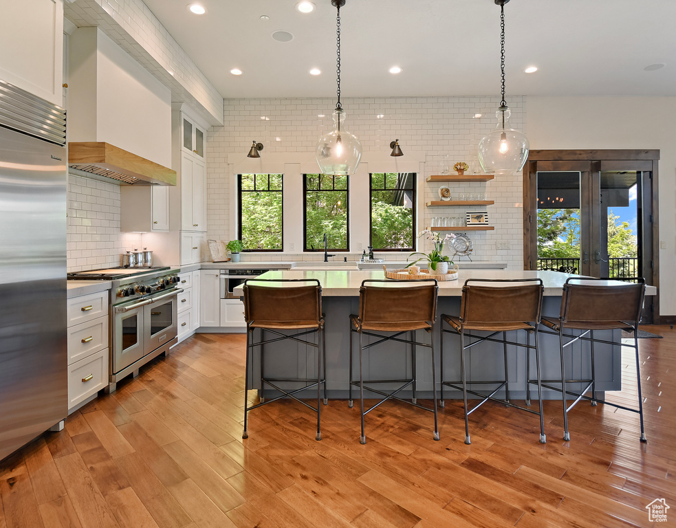 Kitchen featuring premium appliances, white cabinetry, custom range hood, decorative backsplash, and recessed lighting