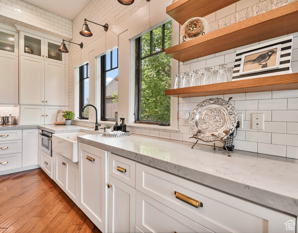 Kitchen with open shelves, tasteful backsplash, white cabinetry, a sink, and light stone countertops