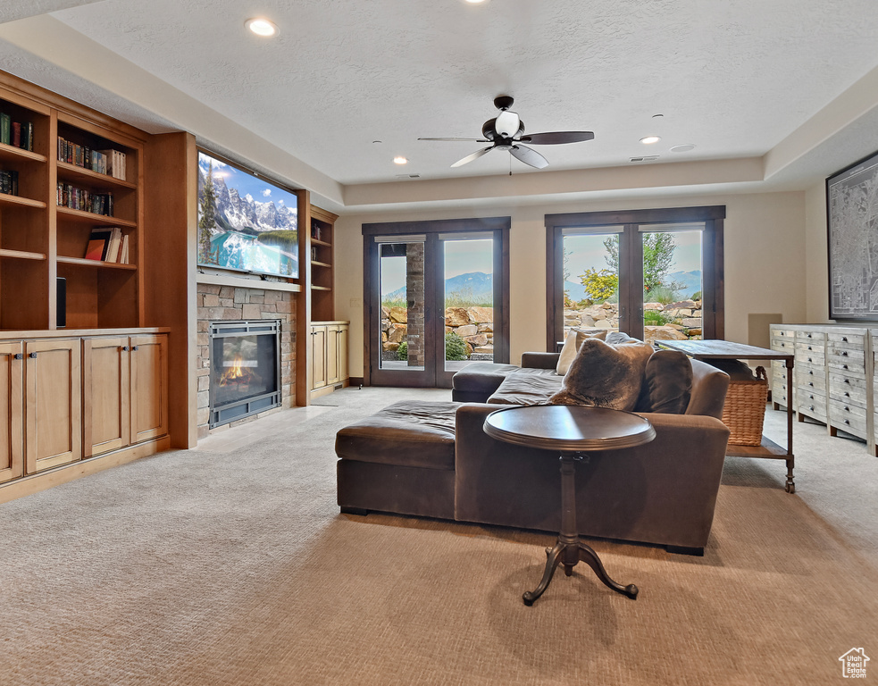 Living room featuring light carpet, a textured ceiling, a stone fireplace, ceiling fan, and recessed lighting