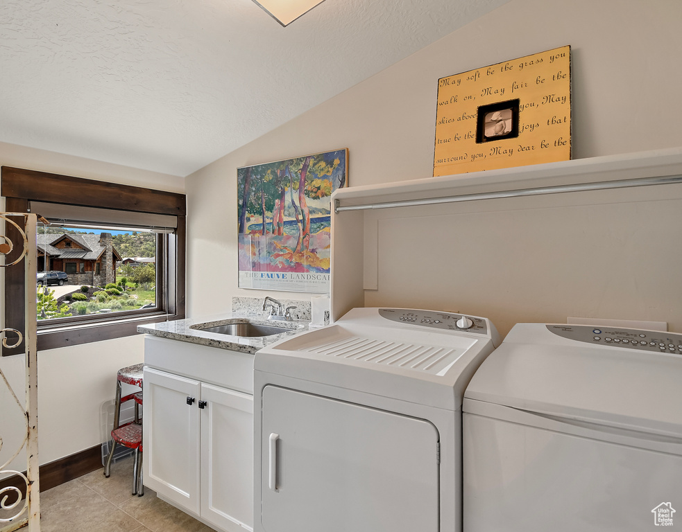 Laundry area with cabinet space, washing machine and clothes dryer, light tile patterned floors, and a textured ceiling