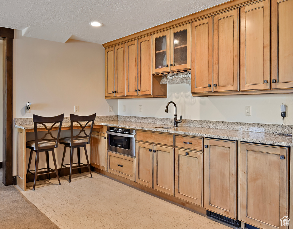 Kitchen featuring stainless steel oven, a sink, a textured ceiling, light stone countertops, and glass insert cabinets
