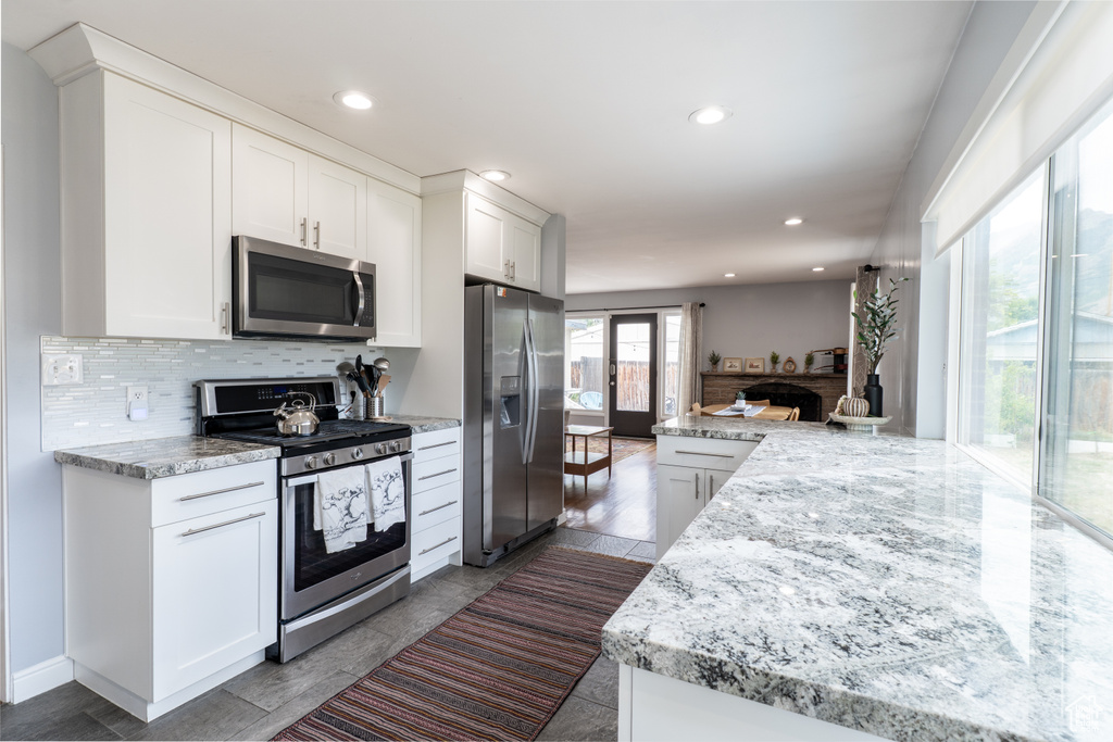 Kitchen featuring appliances with stainless steel finishes, tasteful backsplash, white cabinetry, recessed lighting, and light stone counters