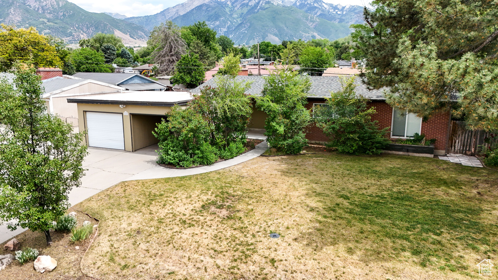 View of front of property with driveway, a mountain view, an attached garage, and a front lawn