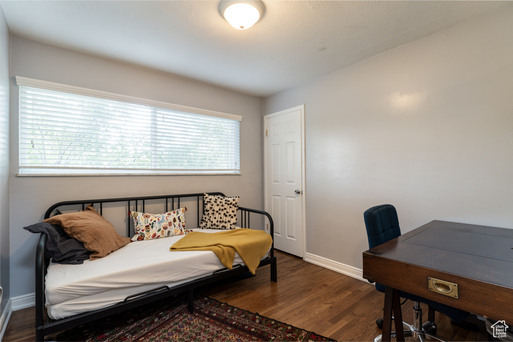 Bedroom with dark wood-style floors, baseboards, and a desk
