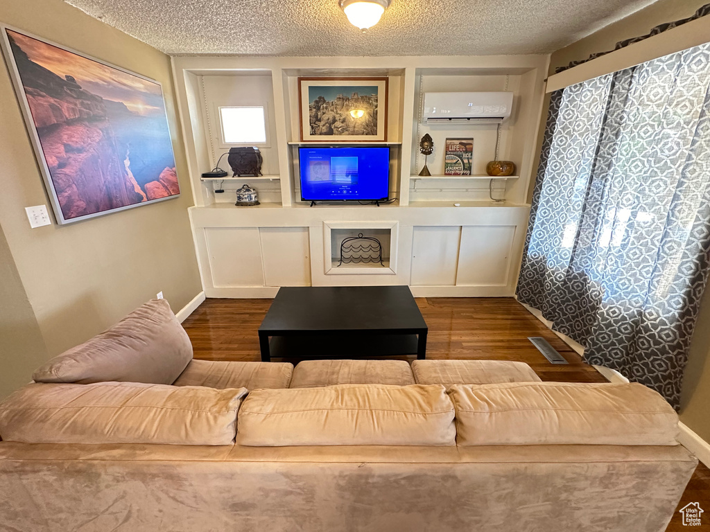 Living area with an AC wall unit, wood finished floors, a textured ceiling, and baseboards