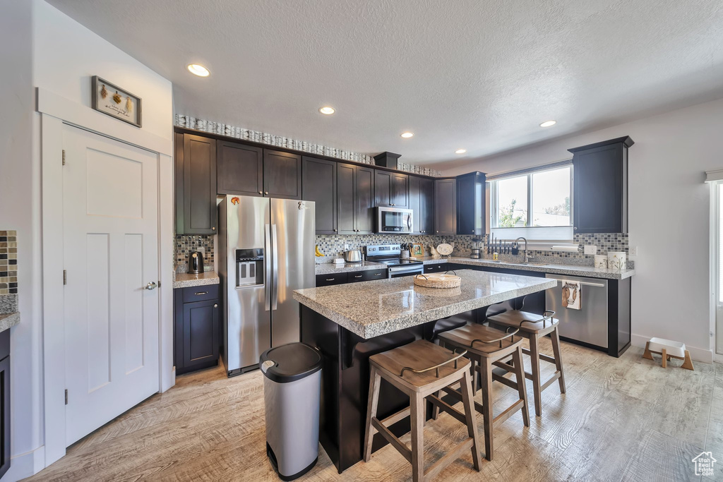Kitchen featuring appliances with stainless steel finishes, decorative backsplash, light wood-style floors, a breakfast bar, and recessed lighting