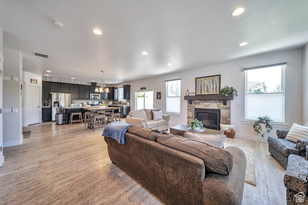 Living area with a chandelier, recessed lighting, a stone fireplace, plenty of natural light, and light wood-type flooring