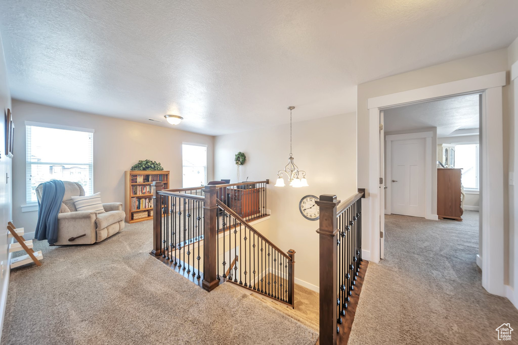 Corridor with an upstairs landing, carpet flooring, a textured ceiling, and a chandelier