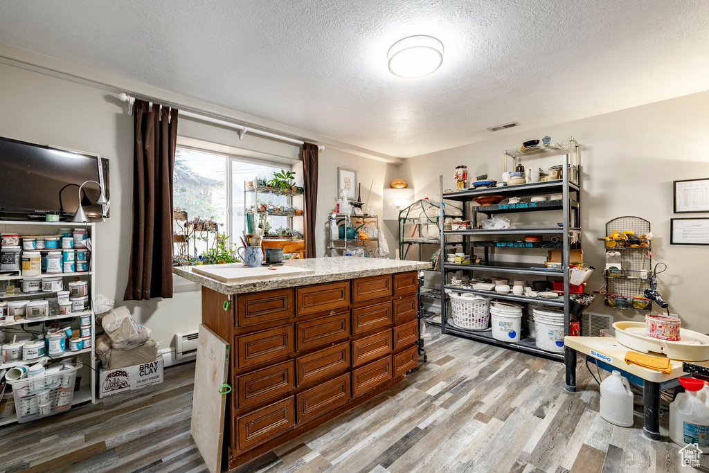 Kitchen featuring light wood-style floors, a textured ceiling, light countertops, brown cabinets, and a baseboard heating unit