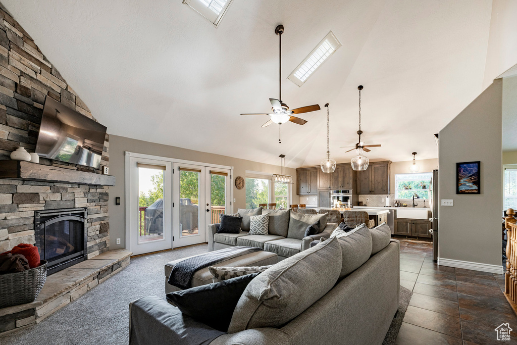Living room featuring a stone fireplace, high vaulted ceiling, ceiling fan, and baseboards