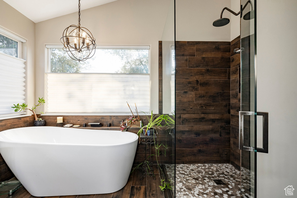 Bathroom featuring a shower stall, a freestanding tub, a chandelier, vaulted ceiling, and wood finished floors