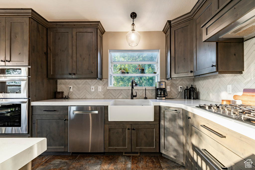 Kitchen with stainless steel appliances, a sink, extractor fan, dark brown cabinets, and decorative backsplash