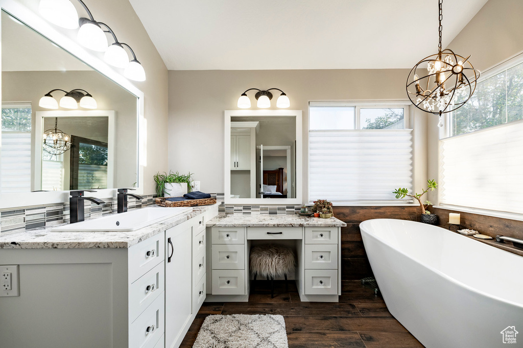 Full bathroom with a chandelier, vanity, wood finished floors, a soaking tub, and vaulted ceiling