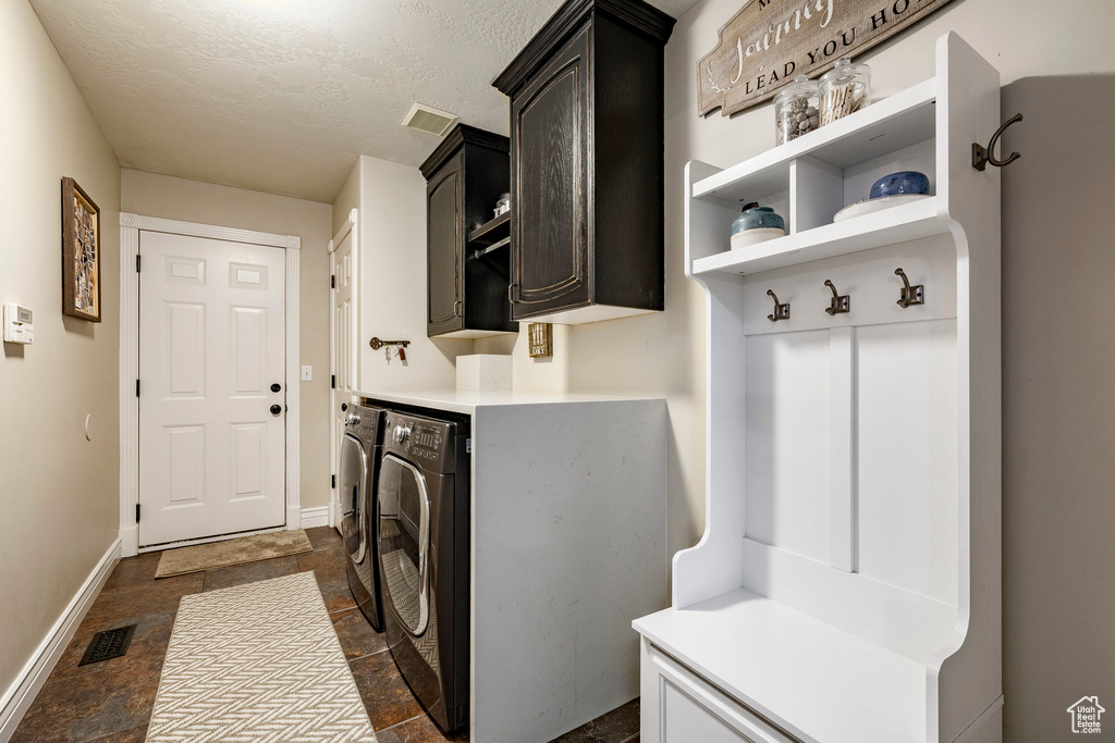 Laundry area featuring cabinet space, washing machine and clothes dryer, dark stone finish floors, baseboards, and a textured ceiling