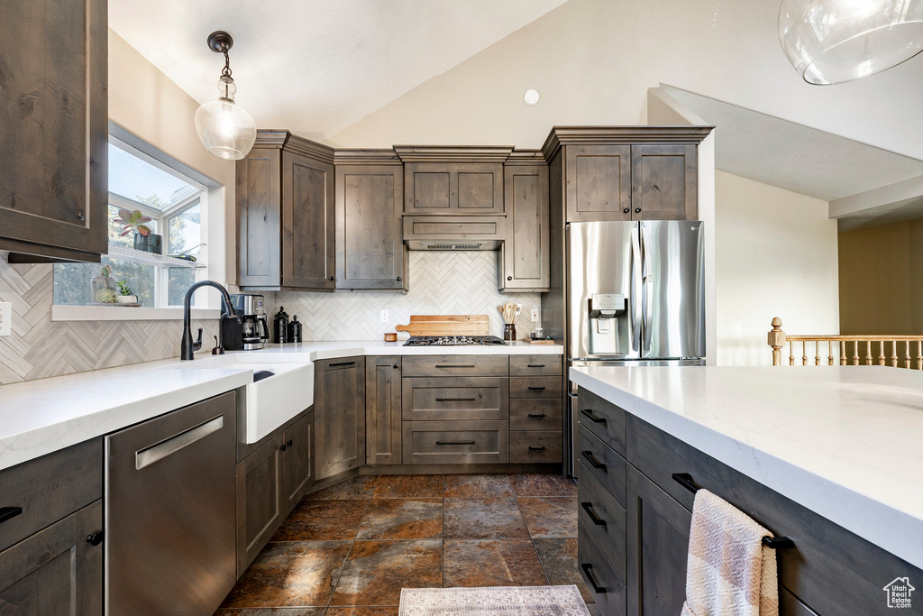 Kitchen with stainless steel appliances, vaulted ceiling, backsplash, light countertops, and dark brown cabinets