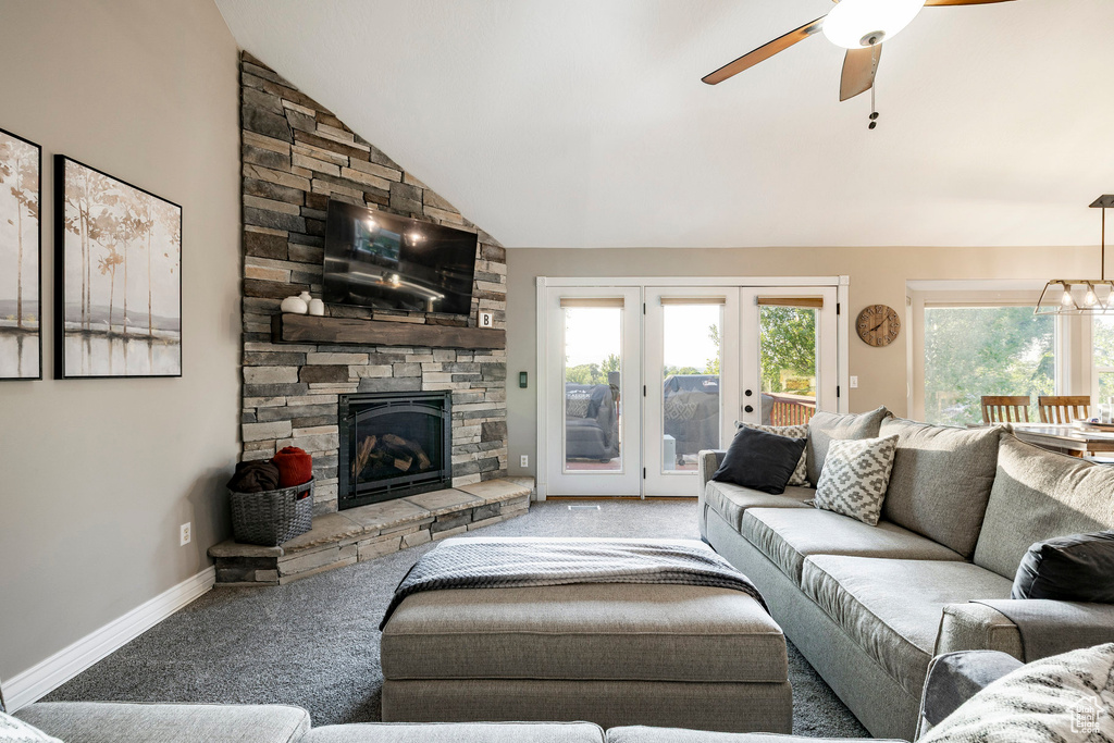 Carpeted living room featuring a stone fireplace, lofted ceiling, ceiling fan, baseboards, and french doors